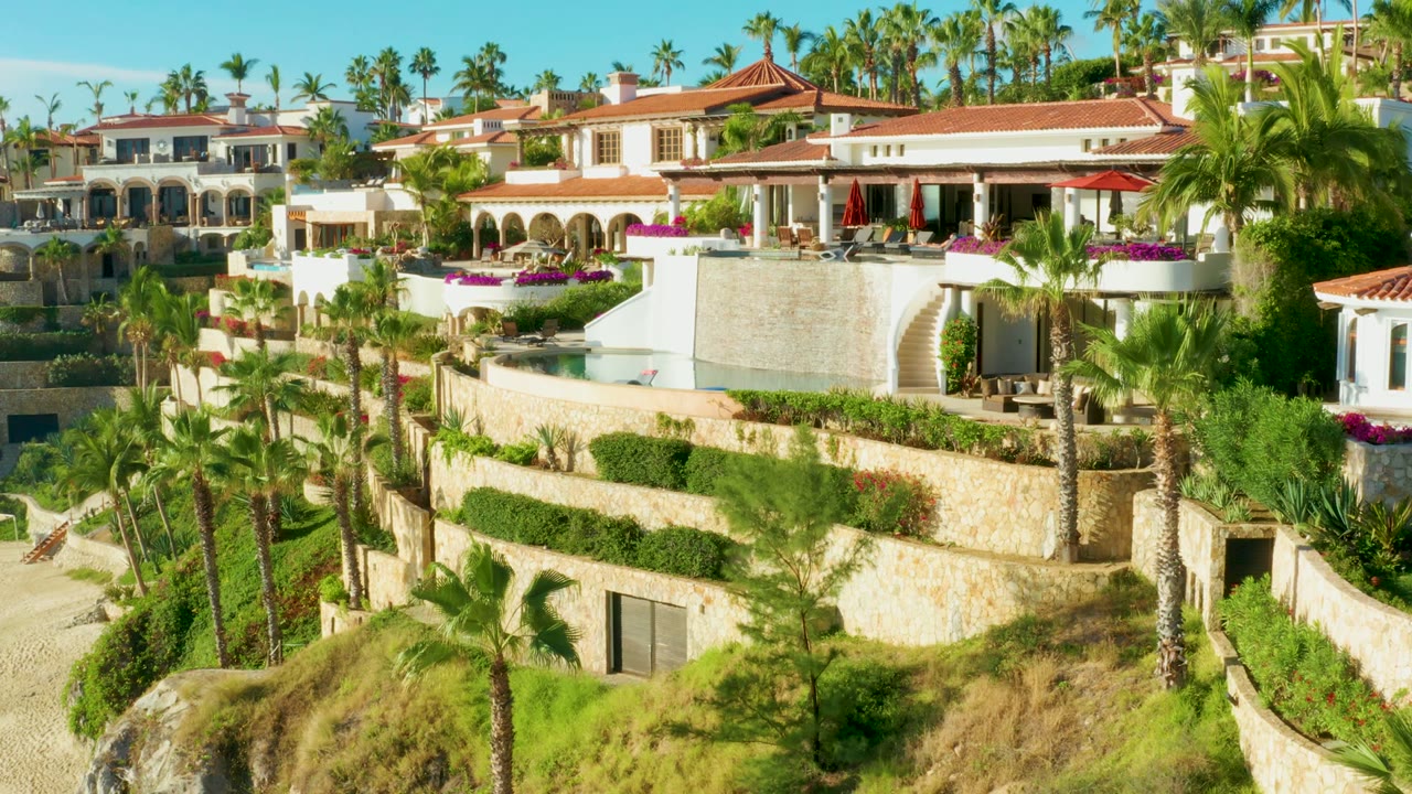 White resort buildings and terraced gardens on a palm-lined hillside.