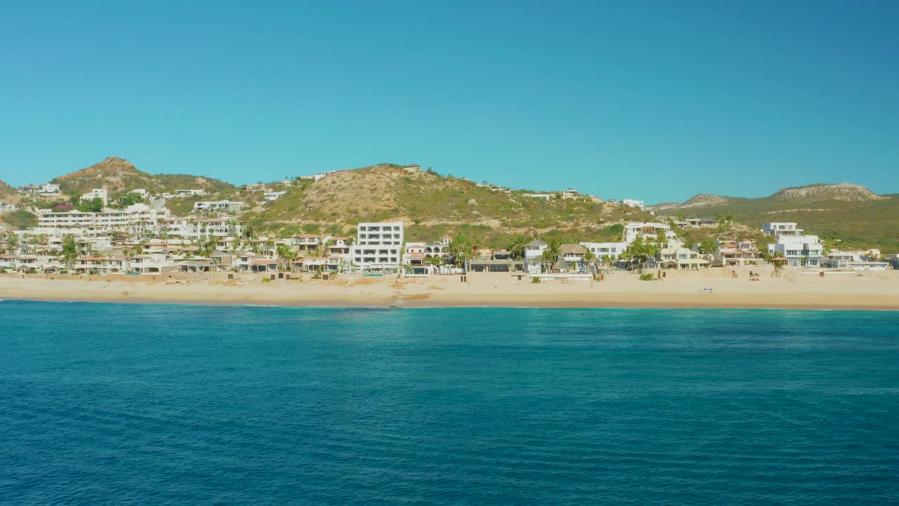 Calm ocean facing a sandy beach with white buildings and hills