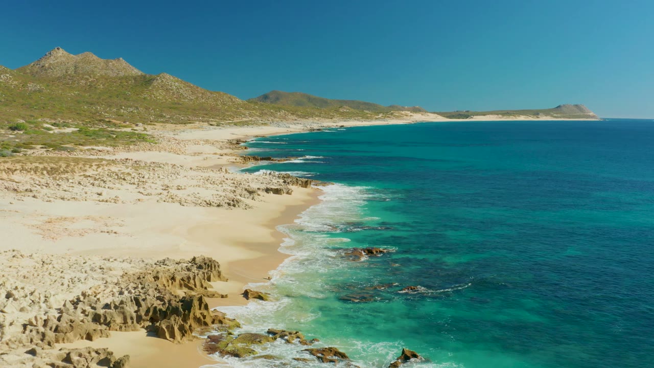 Rocky beach curves beside turquoise water under clear sky.