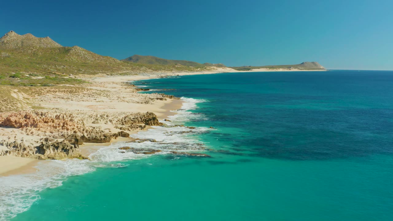 Aerial coastline with white waves breaking along rocks and pale sand.