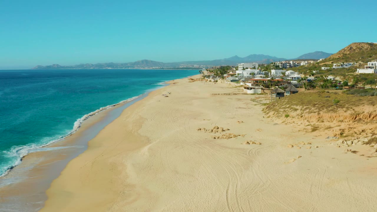 Wide beach and turquoise surf with dunes and white coastal buildings along the right side.