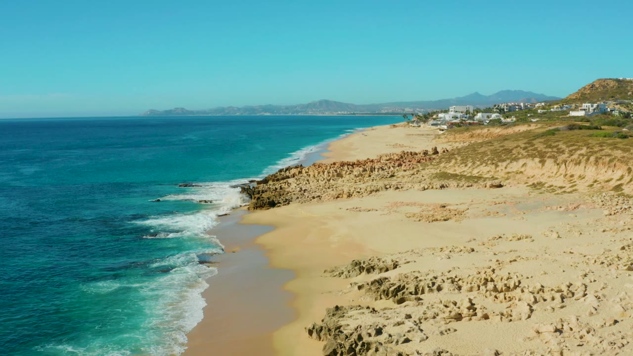 Turquoise waves wash beside a sandy beach and tan rocky shoreline.