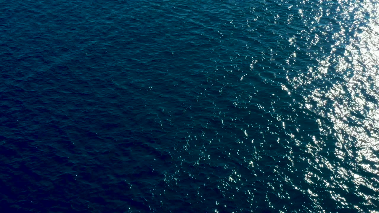 Aerial view of darker blue ocean at Buzzards Beach East Cape with a vertical strip of white sun glint near the right side, no visible people.
