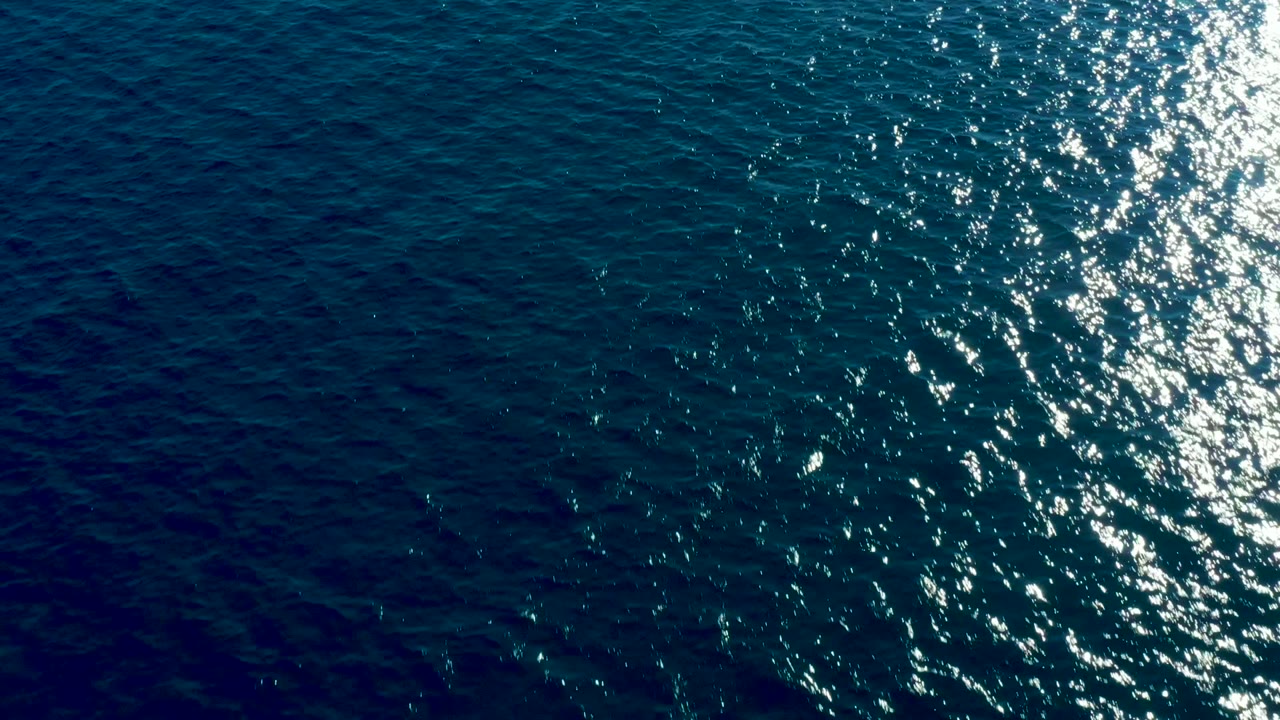 Blue ocean surface in Baja California Sur with dense bright highlights along the right edge and darker rippled water to the left, no visible people.