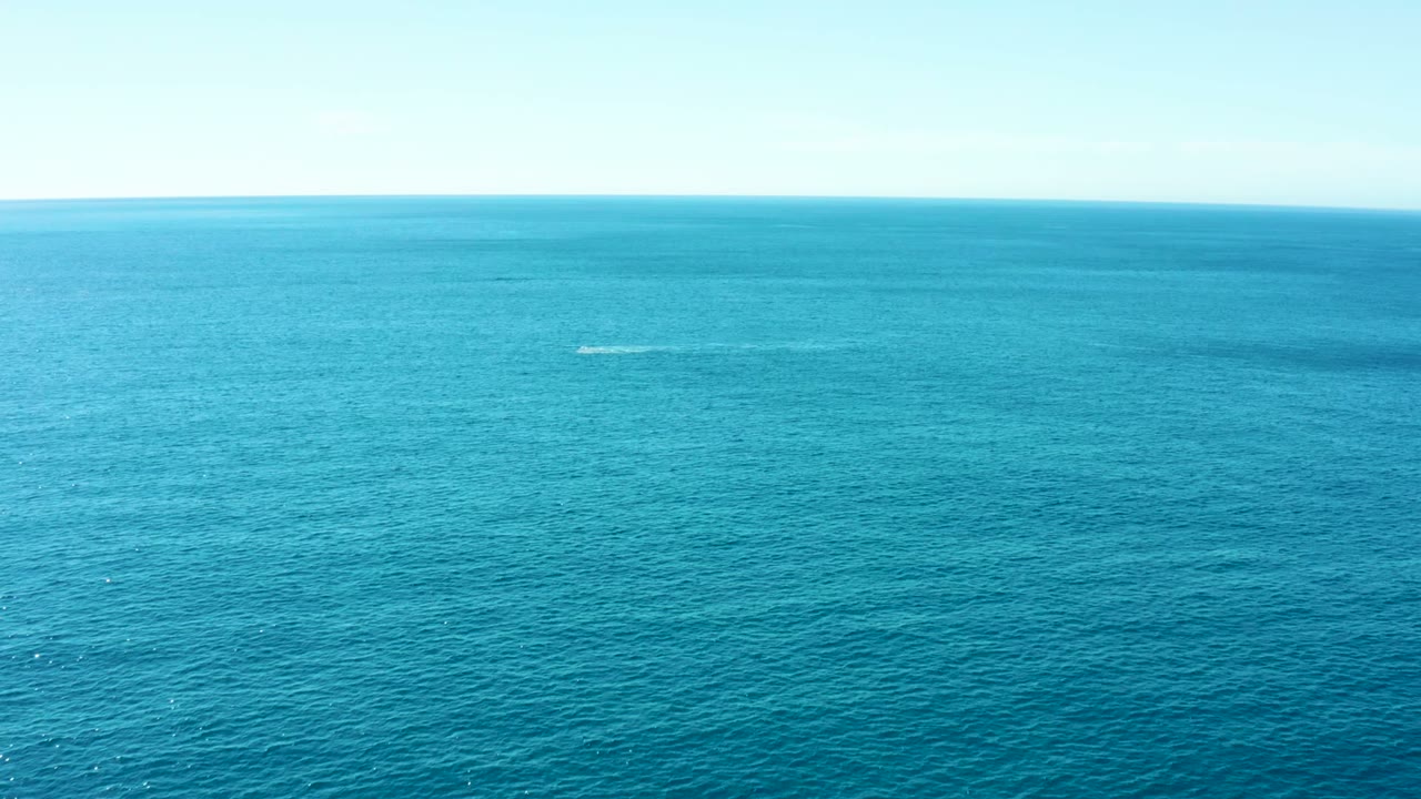 Aerial wide view of blue ocean at Buzzards Beach East Cape, Baja California Sur, with two distant white spray marks near the horizon and no visible people.