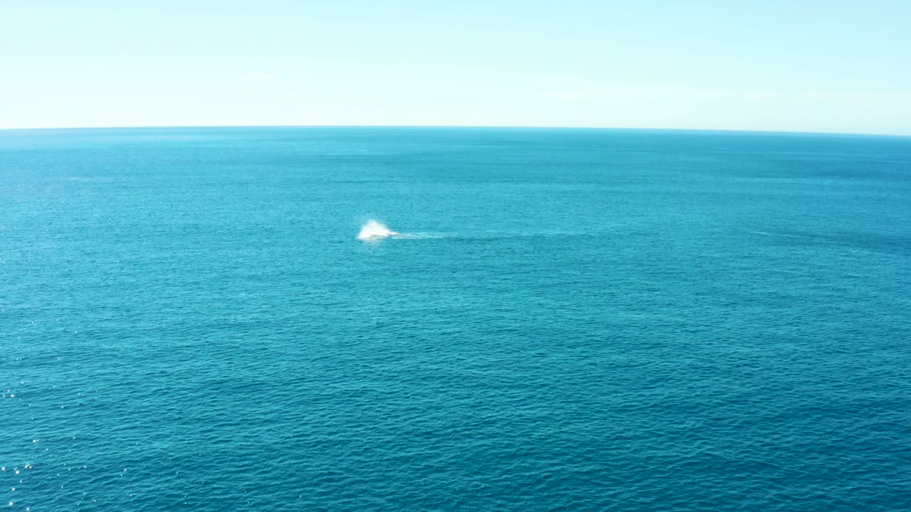 Wide aerial view at Buzzards Beach East Cape, Baja California Sur, with a small white spray trail near the right side of the horizon line and no visible people.