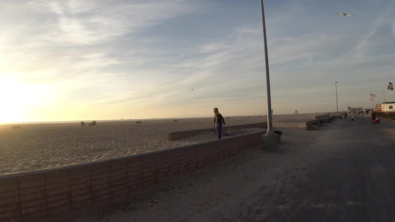 Sunset over a wide beach with a person by the seawall and a path in the foreground.