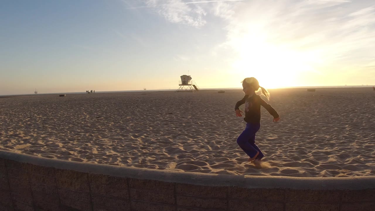 Child continues running on the sandy beach near the wall and sunset.