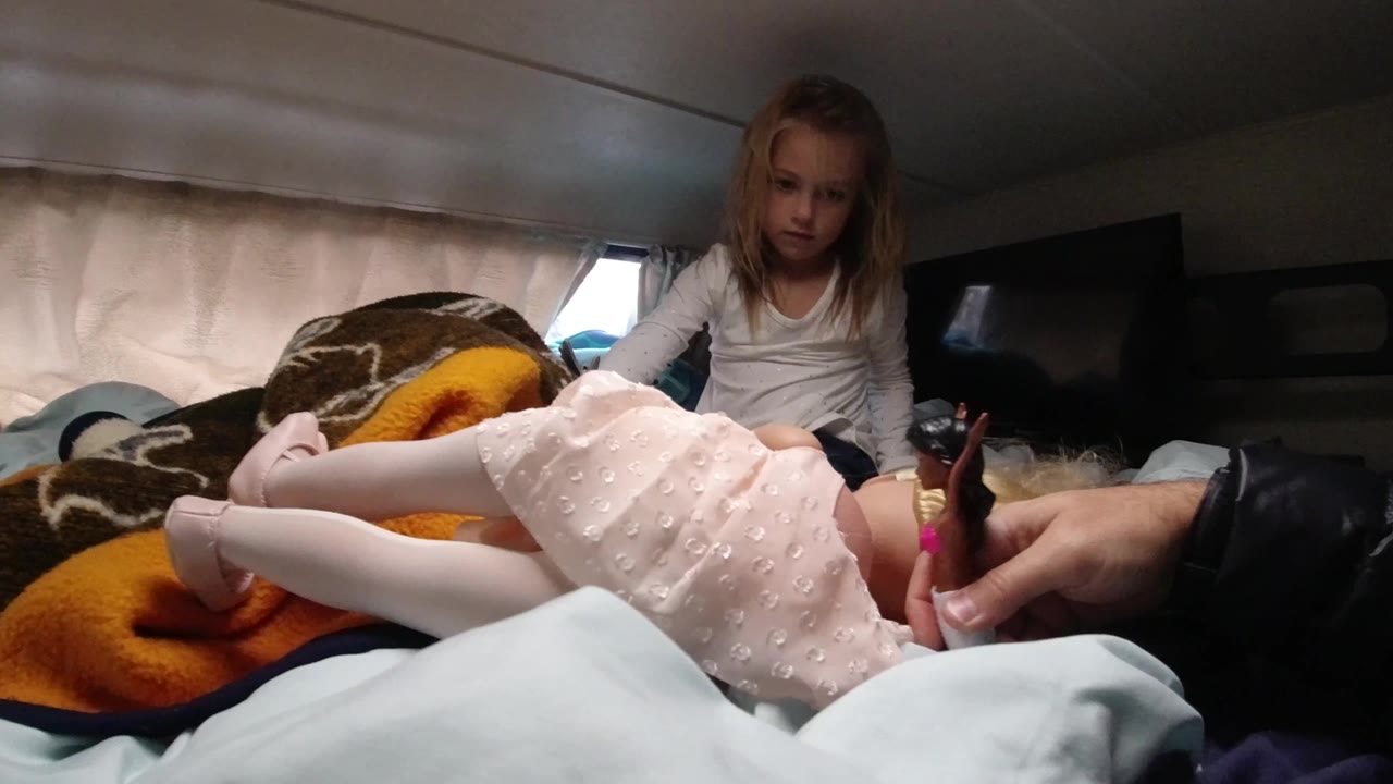 In Santa Maria California, a child in a pink dress and white tights lies across blankets while another young girl watches from the back of the vehicle bed.