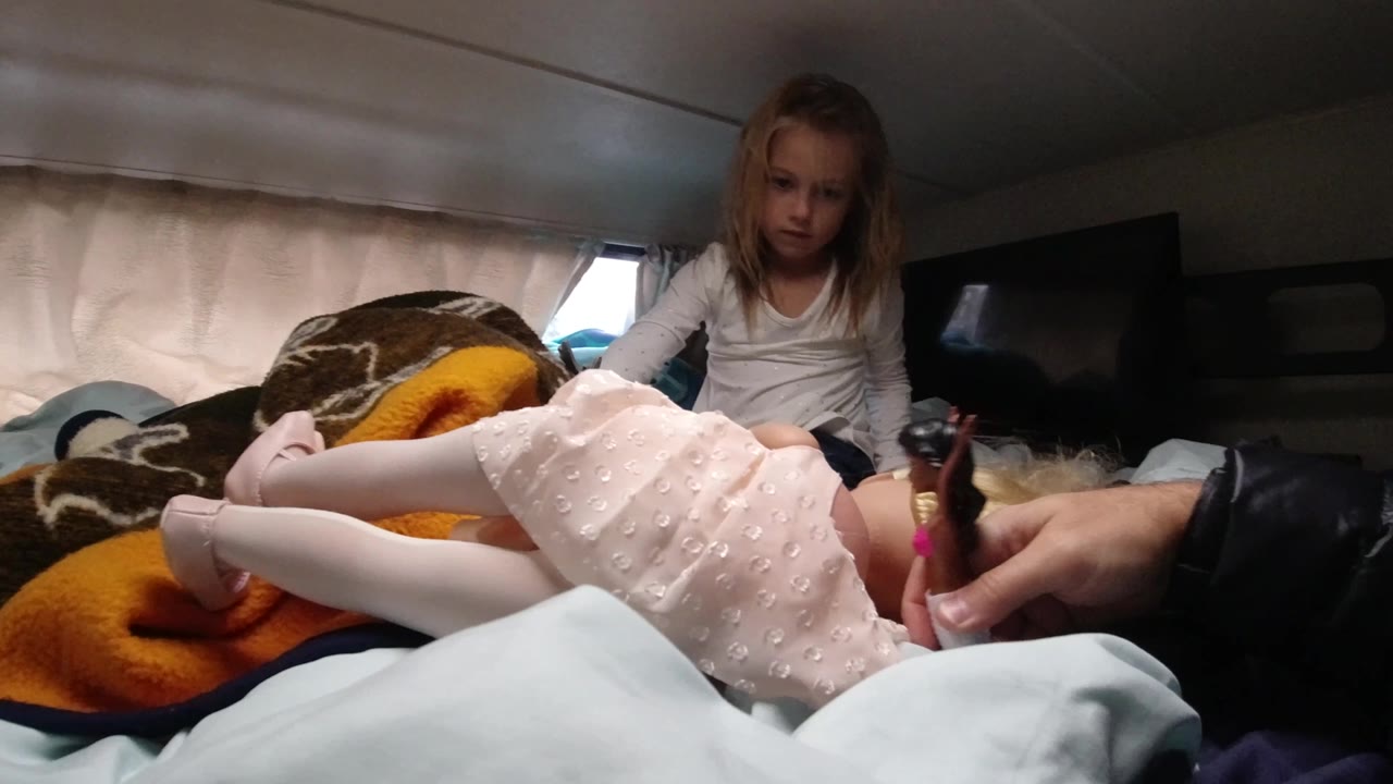Father's hand reaches toward a child lying on blankets as another child sits behind her.