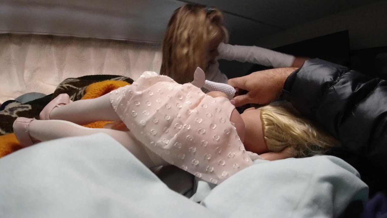 In Santa Maria California, a child in a pale pink dress lies face down on a bed as another young girl sits farther back in the dim interior.