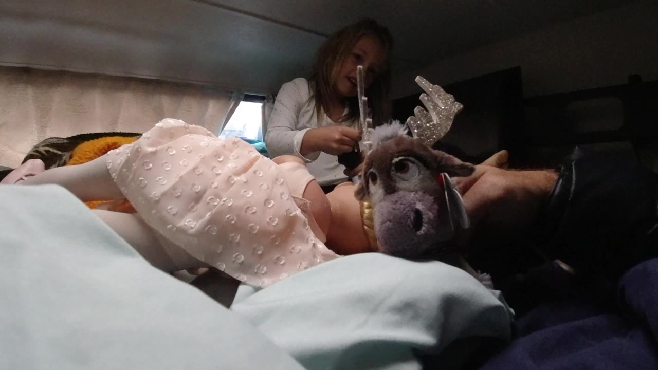 Plush reindeer toy close to a child lying on a bed with a woman behind her.