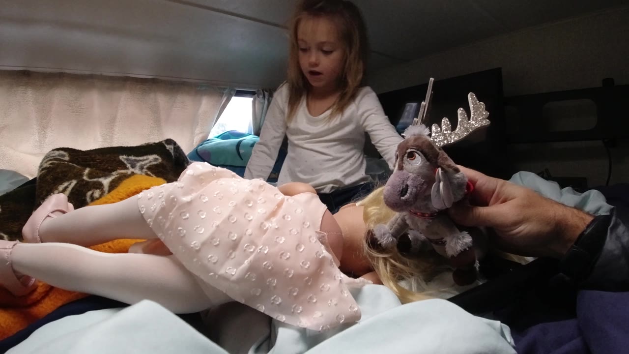At 0:02 in Santa Maria, California, the girl's mouth is open as she watches the stuffed reindeer held at the edge of the bed near the doll.