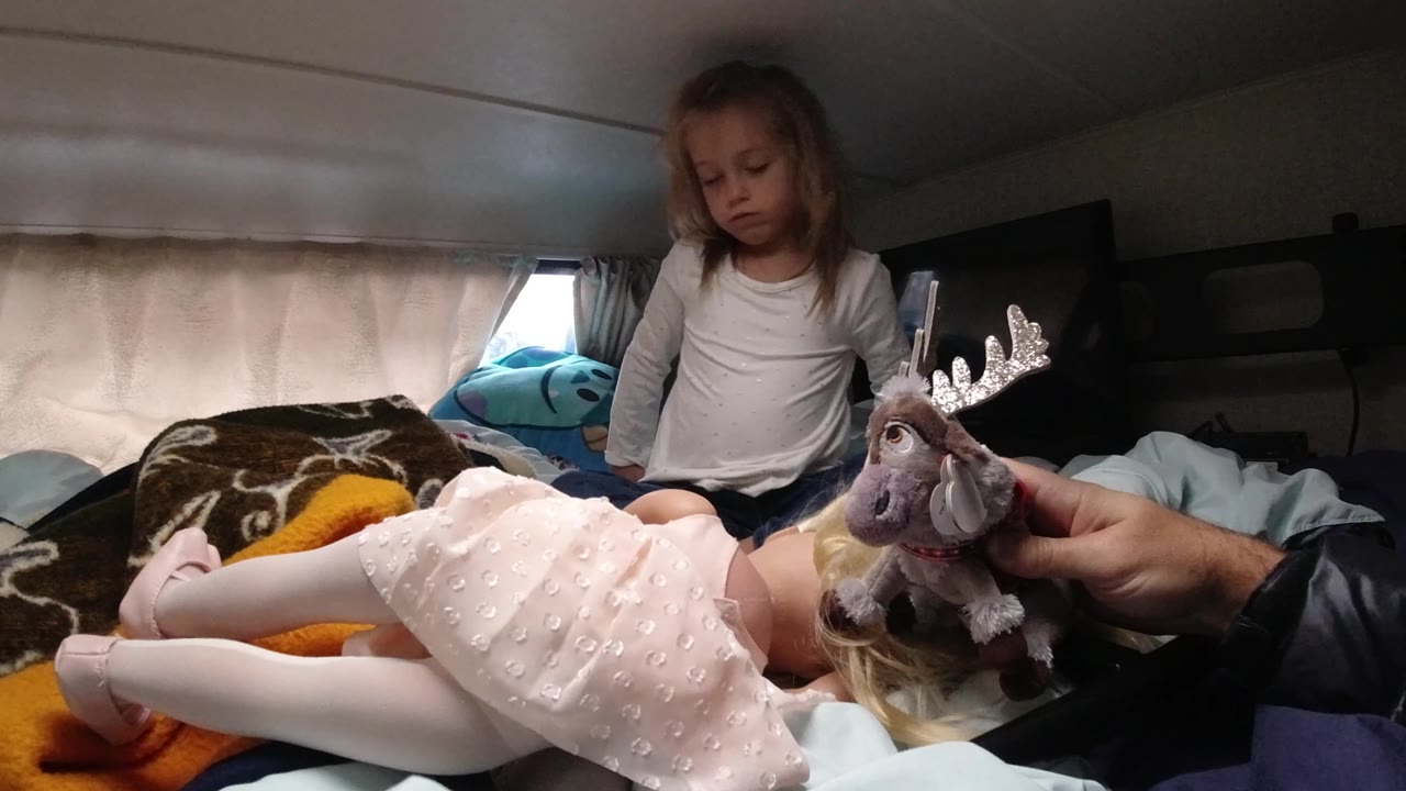 Girl looks down toward a doll as a stuffed moose is held near the doll.