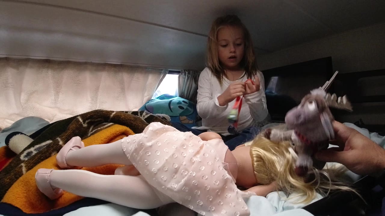 Girl looks down at a red strip while toys rest on the bed.