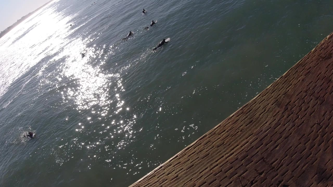 At Pismo Beach California, bright glare reflects on the ocean below a diagonal weathered wooden railing with small distant figures in the water.