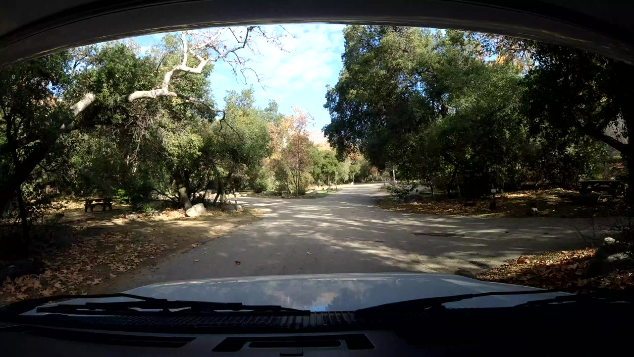 Windshield view in Ojai California showing a paved road curving through a wooded area, with the vehicle hood and wipers in the foreground and no visible people.