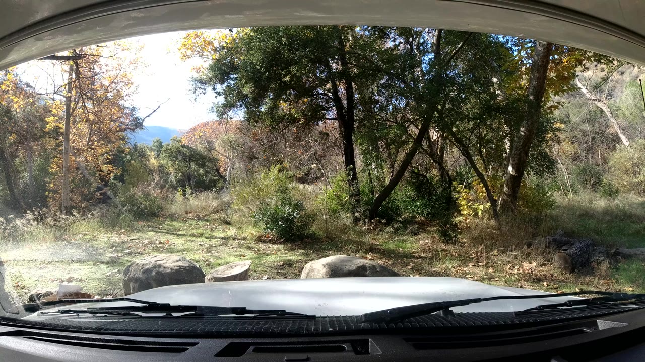Static windshield view of wooded grass and rocks in bright daylight.