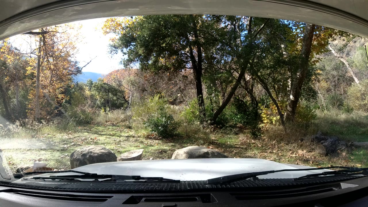 The 0:02 frame shows the car hood lower in frame with wipers below a sunlit Ojai California mix of grass, shrubs, rocks, and autumn-tinged trees, with no visible people.
