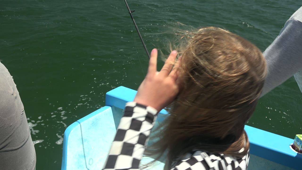 Girl raises a hand to her hair while a fishing line drops toward the water.