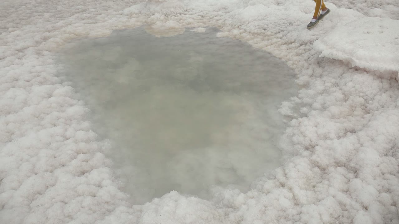 At 0:00 in Guerrero Negro BCS Mexico, the frame looks down across white salt crust and a pale shallow pool, with only the lower legs of a child visible near the top edge.