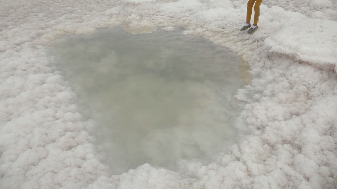 White salt flat and shallow pool with a child's legs near the upper edge.