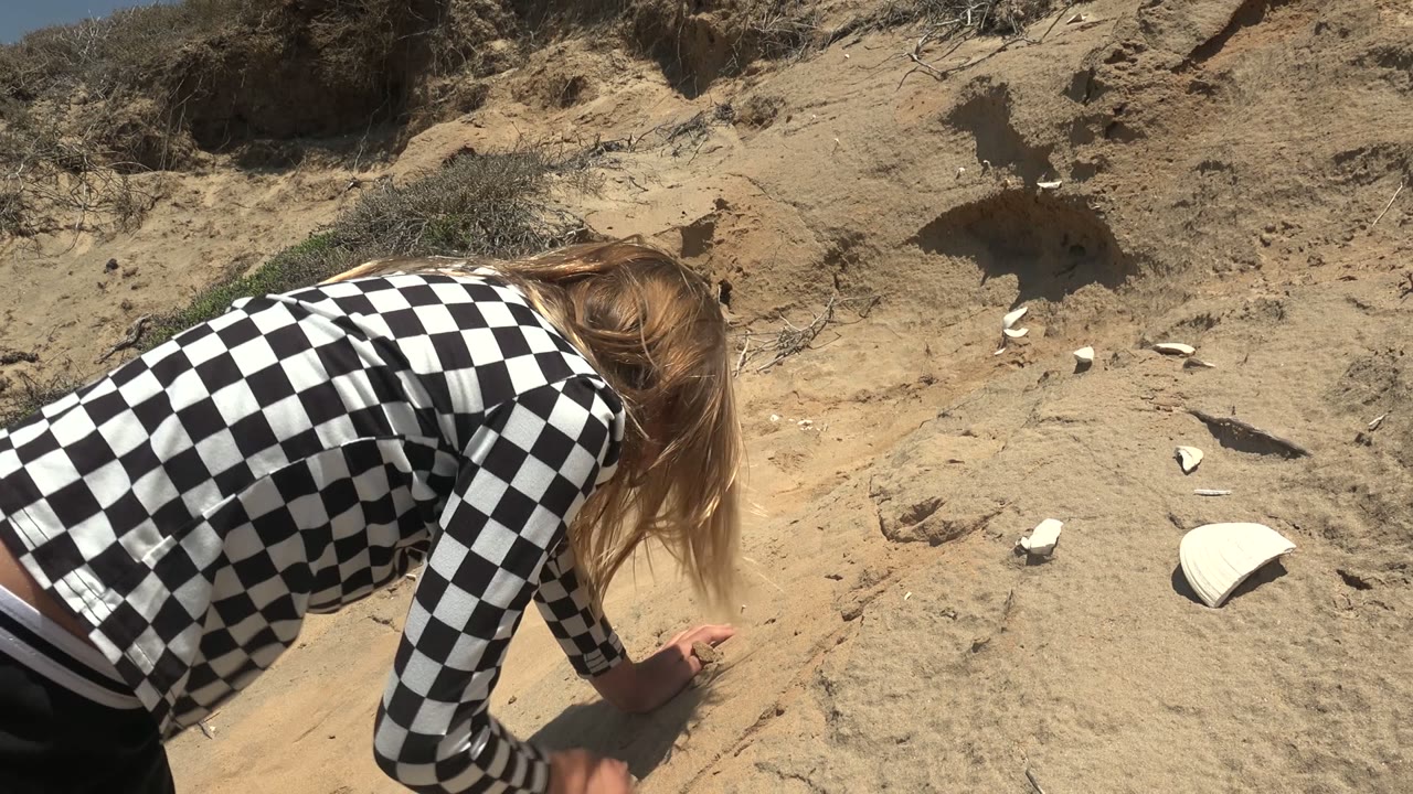 Person reaches toward sand on a dry slope.