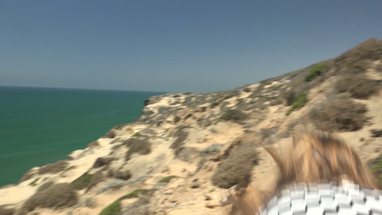 Sandy coastal bluff and turquoise ocean with the hiker low in frame.