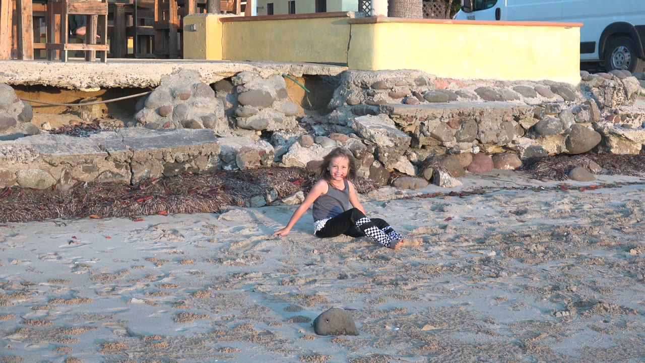 Child seated on sand with rocky shore behind her.