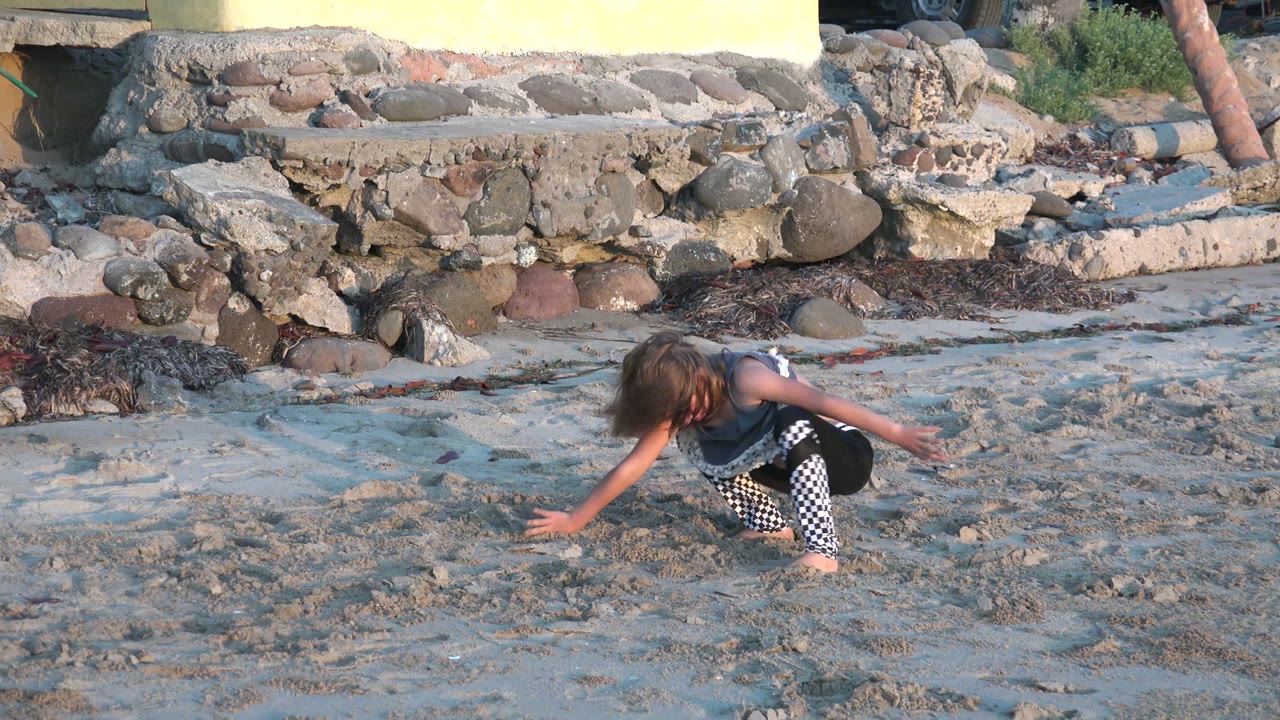 Girl crouched with arm extended on beach sand