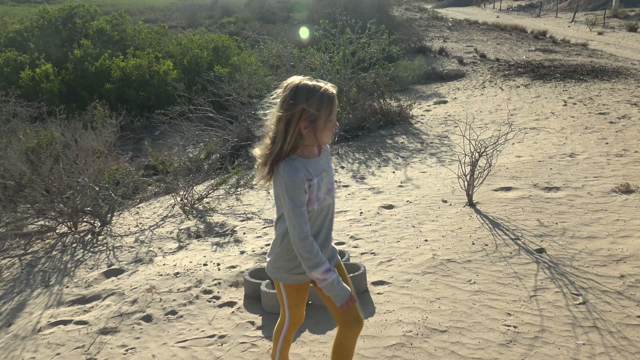 Young girl walking past desert shrubs on rippled sand.