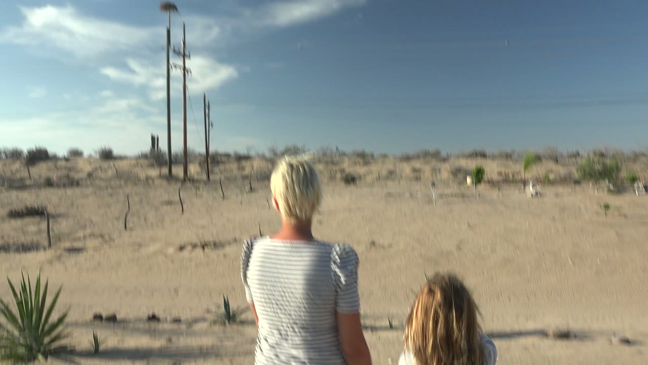 Two people walking toward utility poles in an open desert landscape.