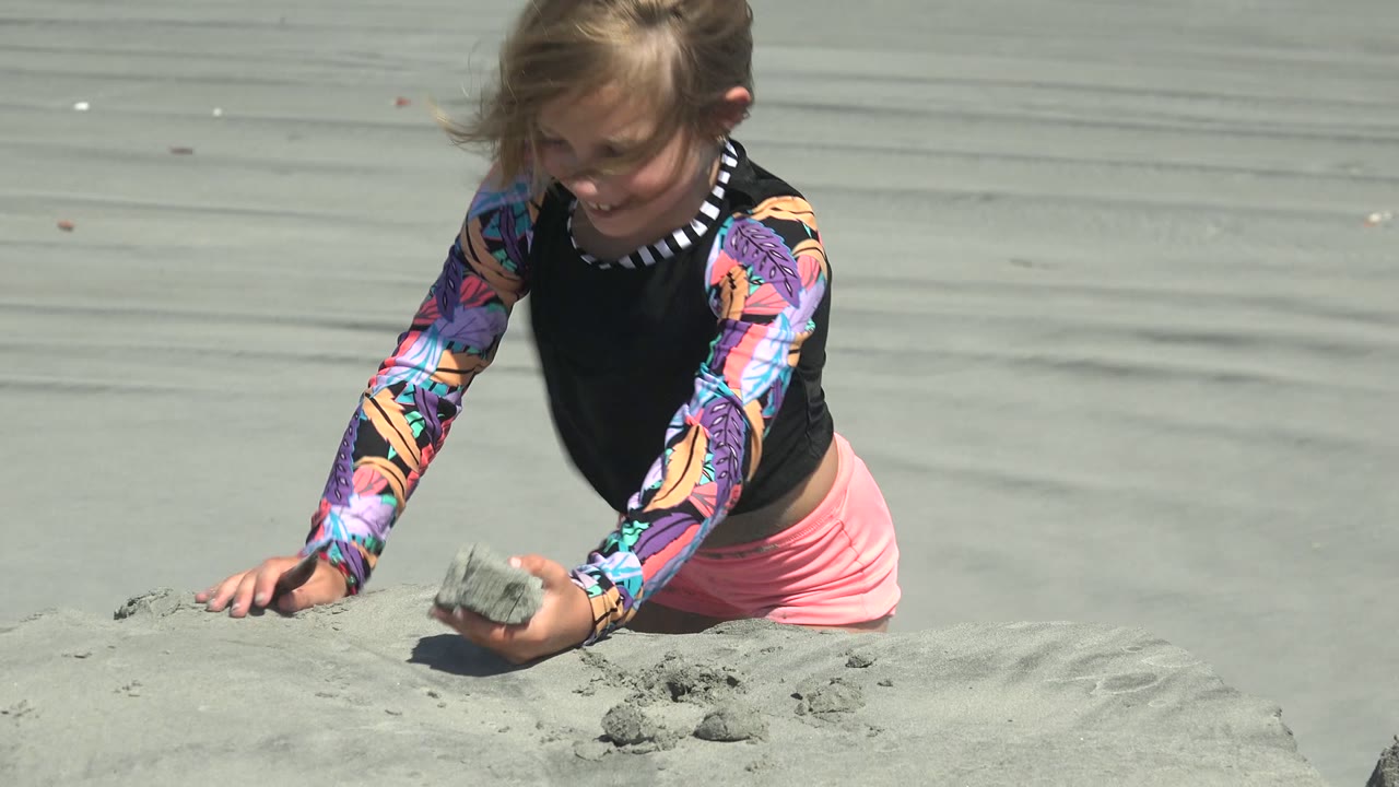 Young girl kneeling and holding a clump of sand.