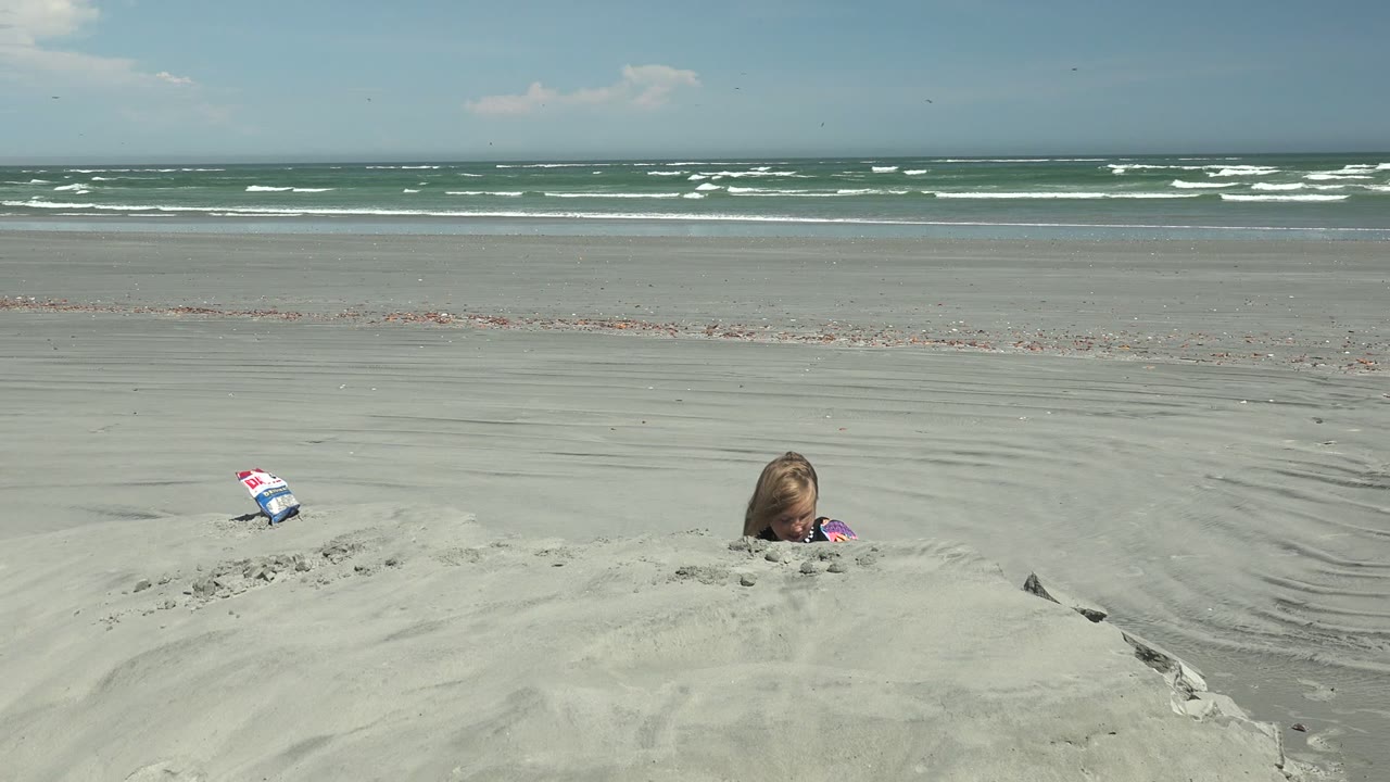 At La Bocana BCS Mexico, a child is partly hidden behind a pale sand mound while ocean waves break along the far horizon.