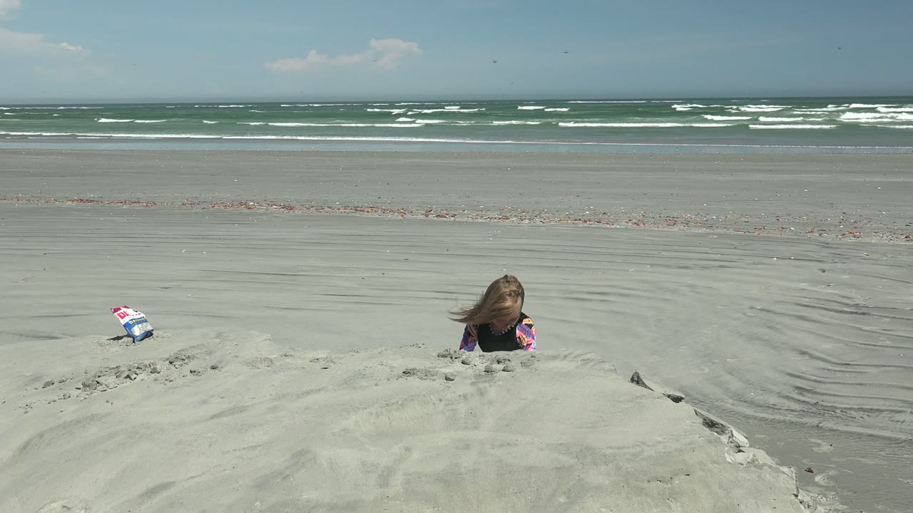 Child's head above sand on a wide beach with waves behind.