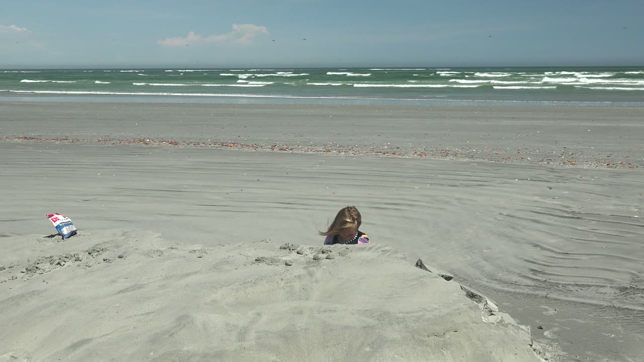 At La Bocana BCS Mexico, the child dips lower behind the sand mound while a small toy or bag sits to the left and surf rolls in the distance.