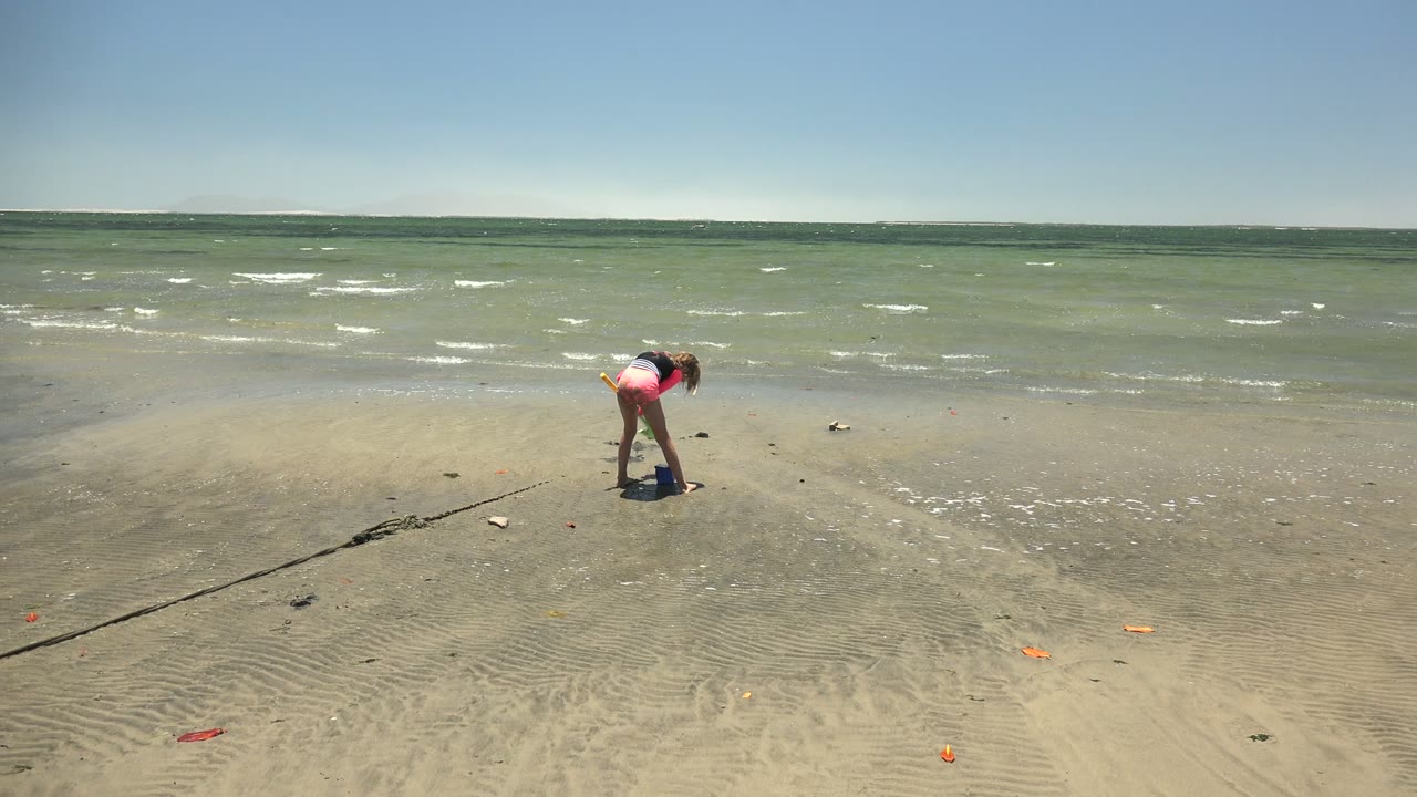 Child standing bent over on sandy beach with waves behind.