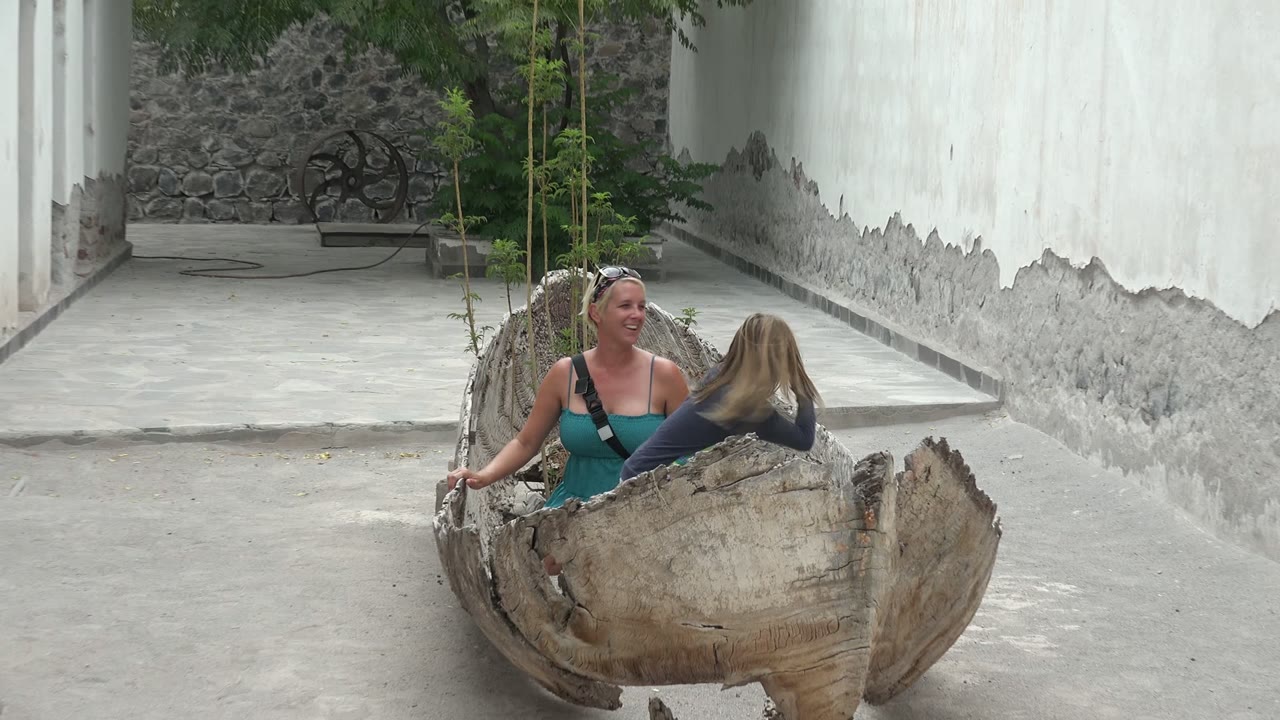 Adult woman looking toward a child inside a large wooden bowl.
