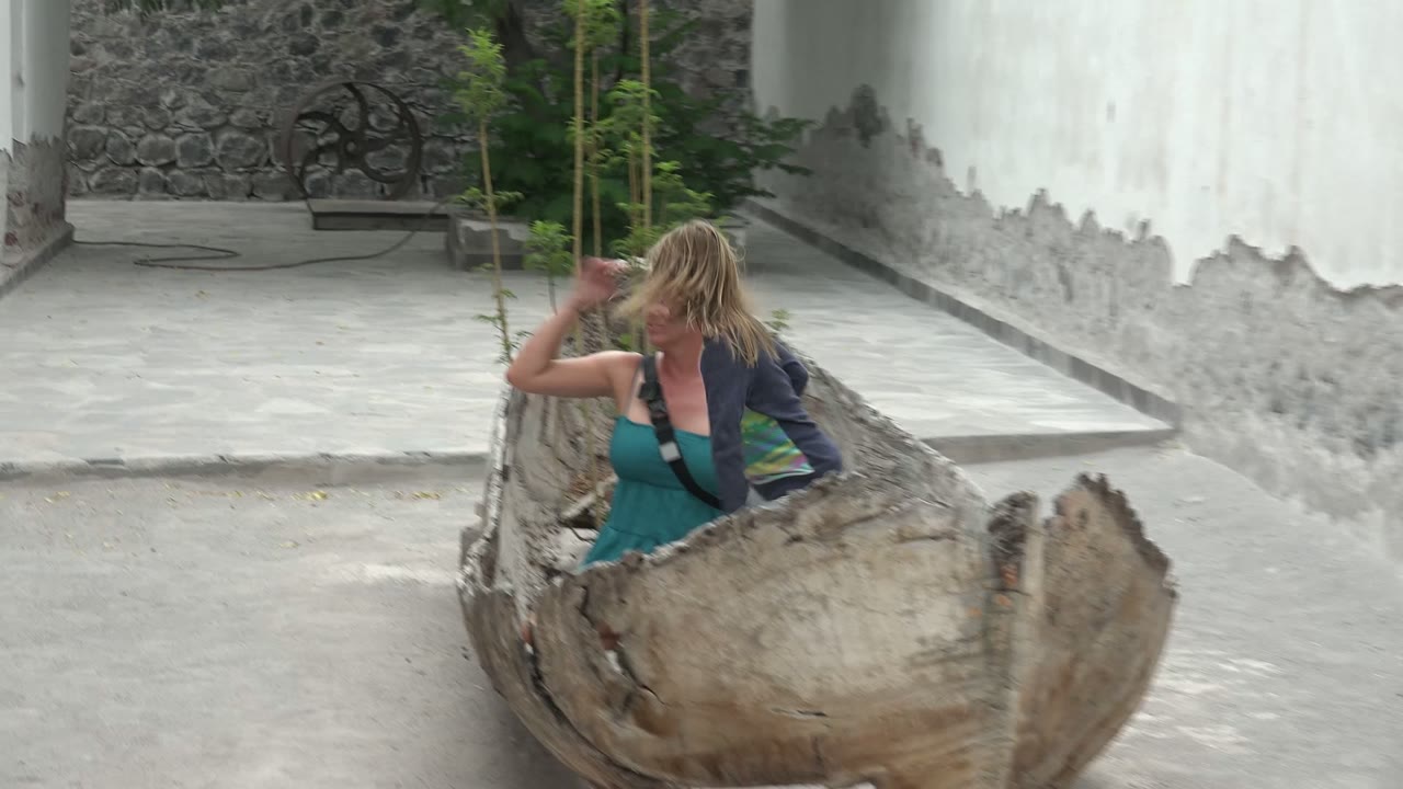 In Mulege BCS Mexico, the adult woman shifts position inside the large wooden bowl as the child is mostly obscured by the foreground rim and the white wall runs behind them.