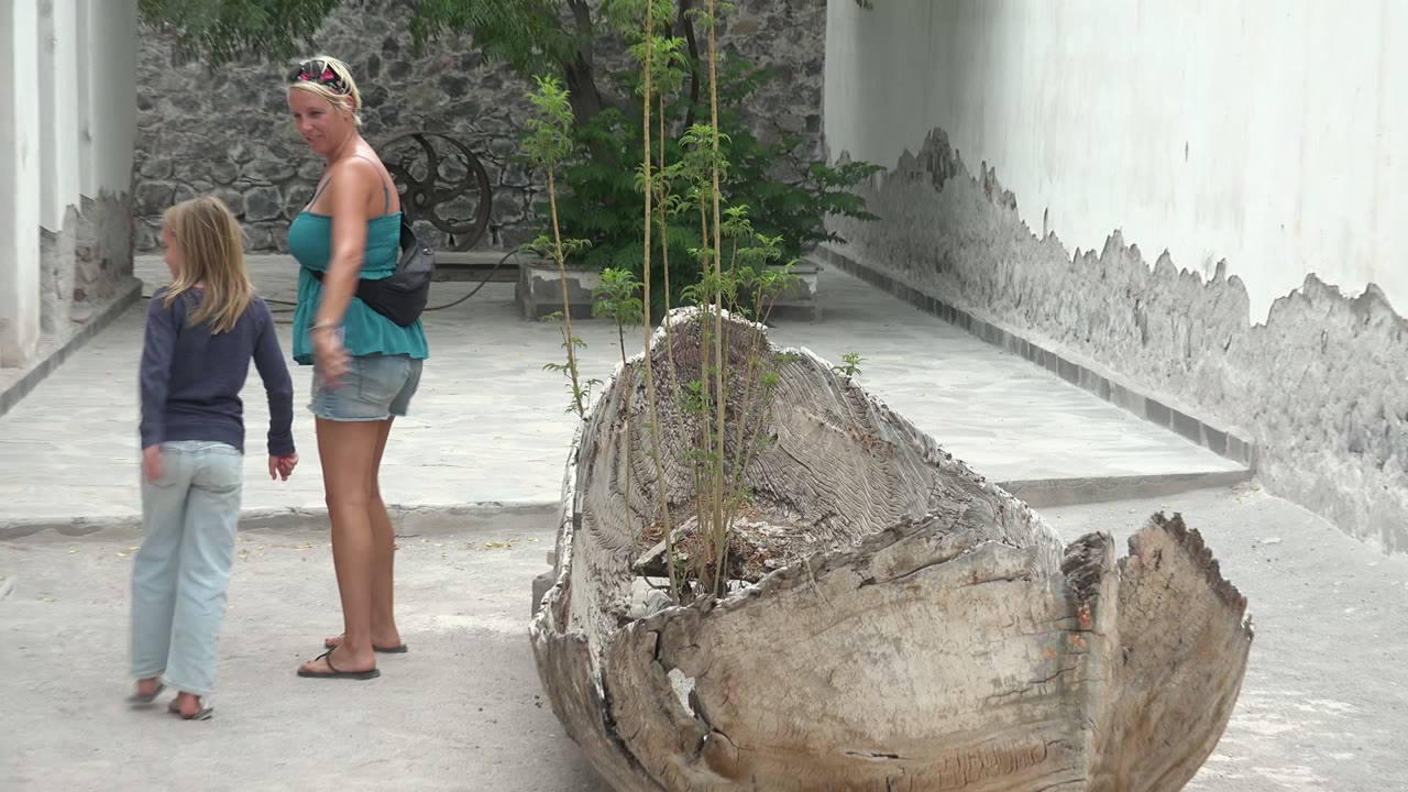 Woman and child walking beside white courtyard walls and a wooden planter.