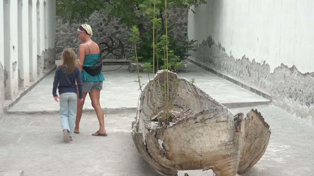 At 0:02 in Mulege BCS Mexico, the woman and child are seen from behind walking toward the far end of the courtyard, with the broken wooden planter in the right foreground.