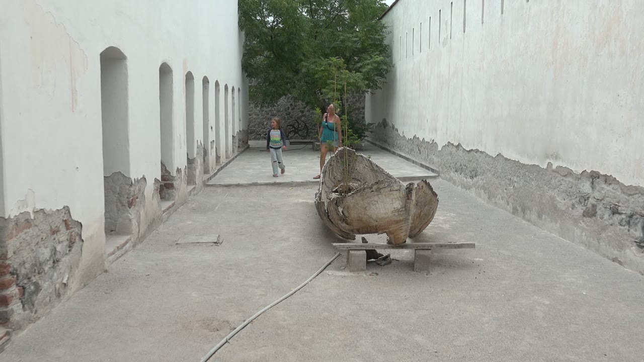 Two people walking closer through a narrow courtyard beside white arches.