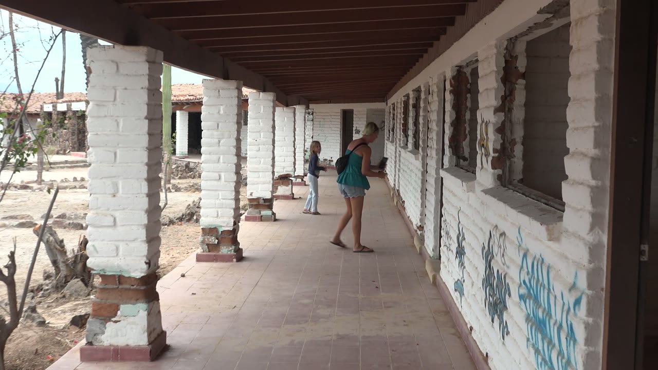 At 0:00 in Mulege BCS Mexico, a woman leans toward a white brick wall while a child stands farther back under the covered corridor.