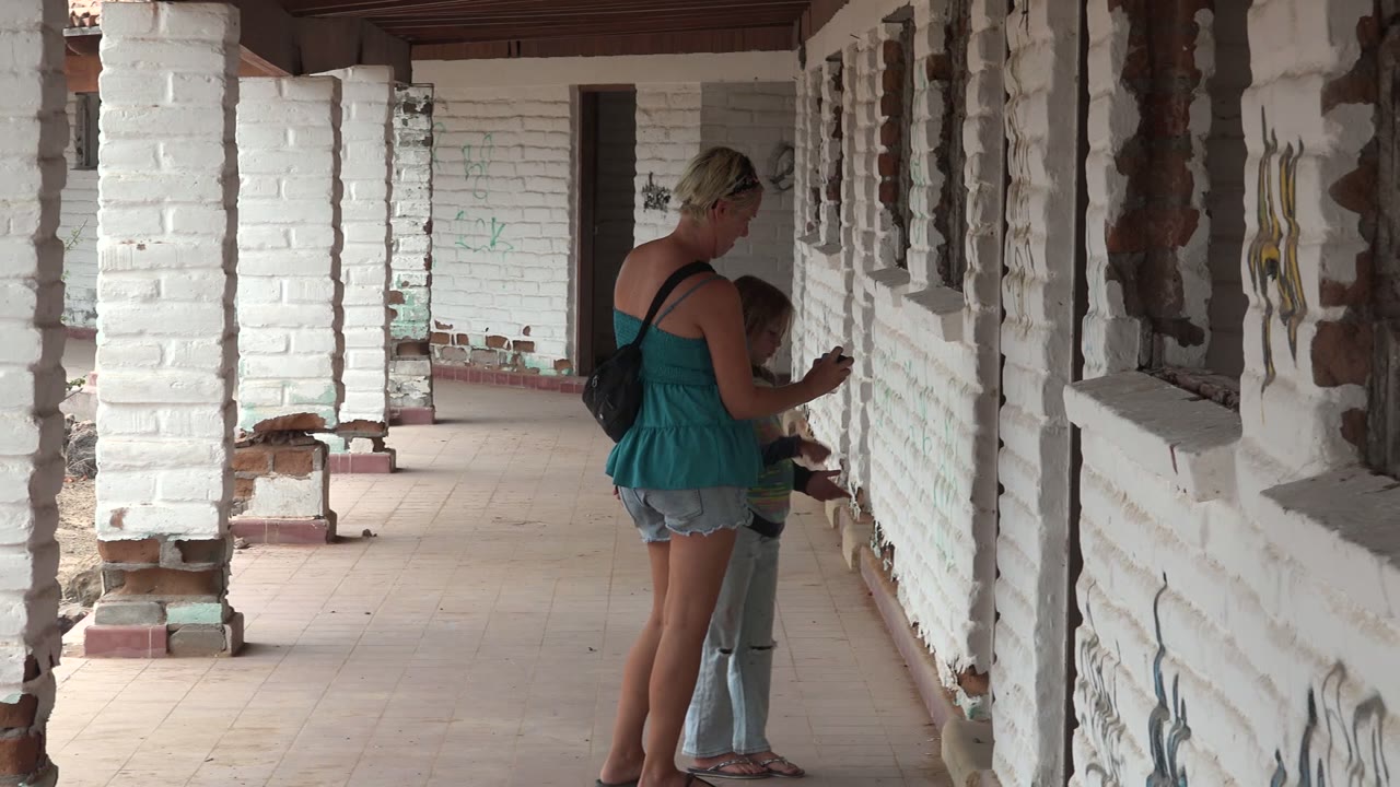 The pair are framed between white brick columns and a graffiti-marked wall, still facing the corridor side in Mulege BCS Mexico.