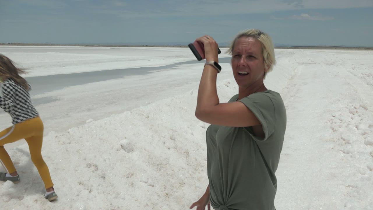 Foreground woman holding a phone while another person steps on the salt flat.