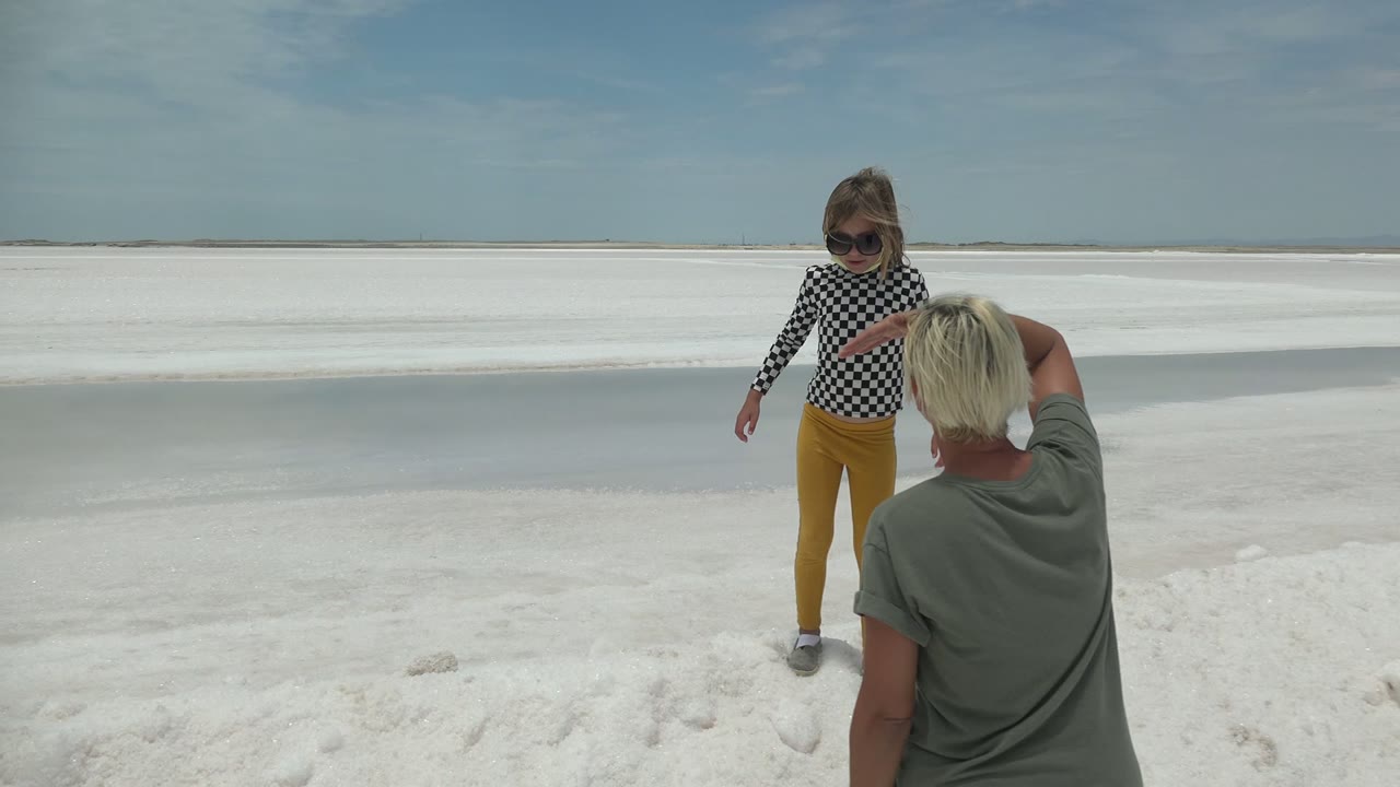 Child faces an adult holding a phone on bright white ground.