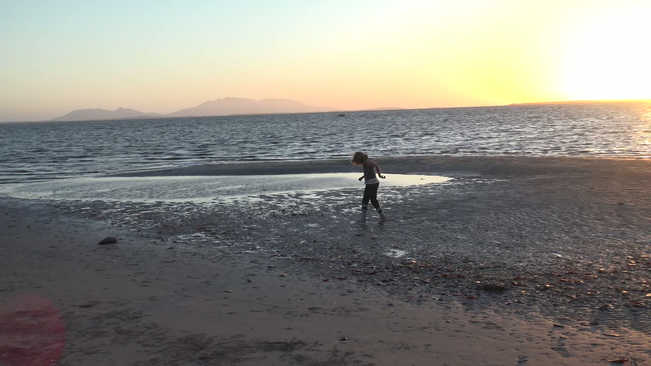 Child walking across wet pebbly beach with ocean behind
