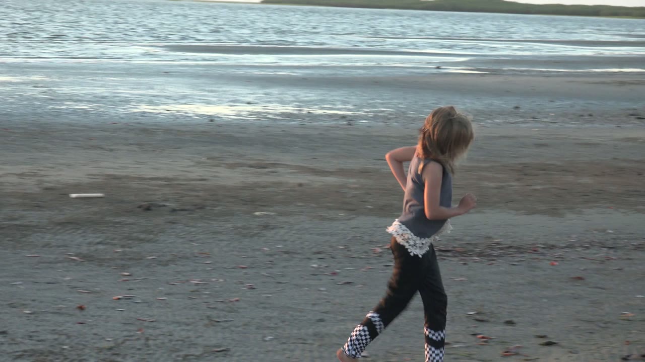 A child runs across dark wet sand near gentle ocean water in San Carlos BCS Mexico, with the horizon and shoreline flats behind them.