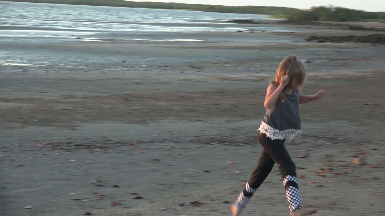 Child running across broad beach with water behind.