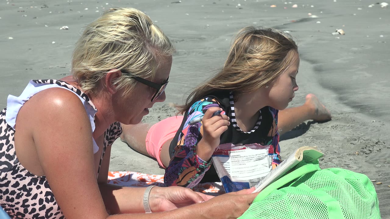 In La Bocana BCS Mexico, the child turns their head to the right while the woman stays low on the sand near a green mesh beach bag and small packet.